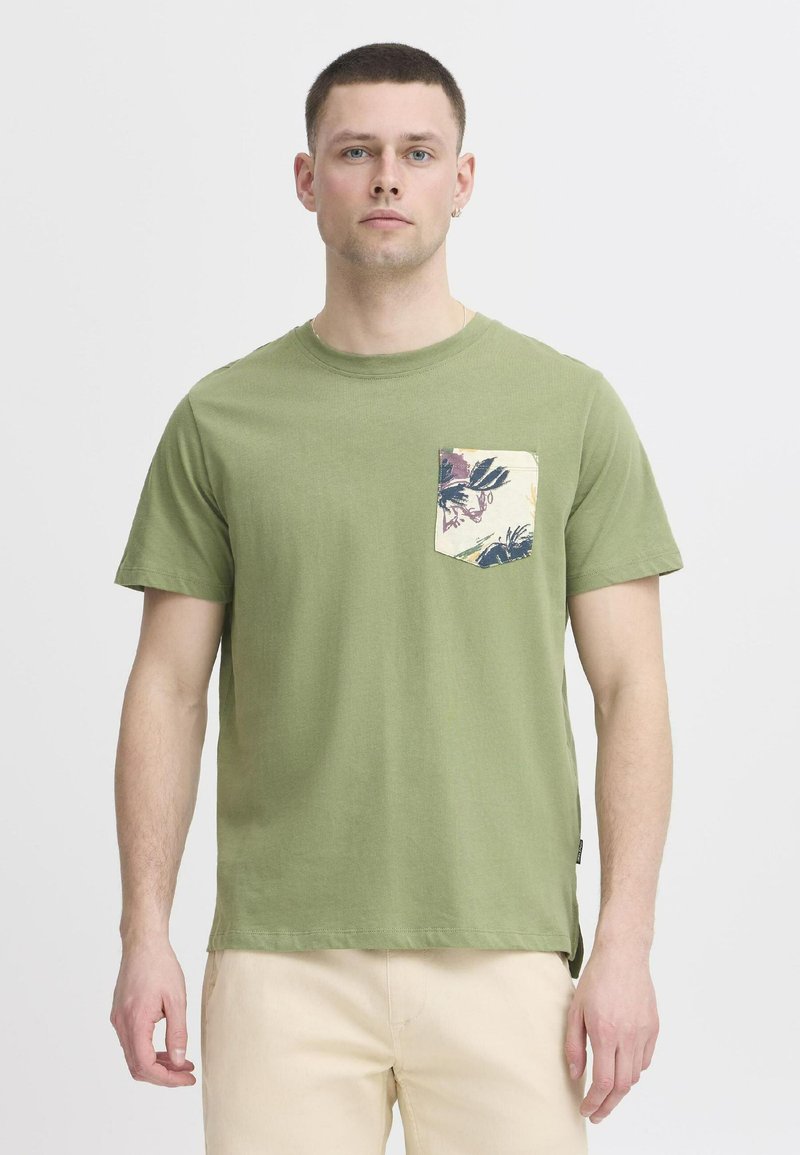 Olivově zelené bavlněné tričko s kulatým výstřihem a krátkými rukávy, které má vzorovanou kapsu v krémové barvě s květinovými detaily.