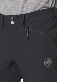 Zwarte technische broek met een zachte textuur, voorzien van een ritssluitingzak, metalen knopen en een logo op het onderbeen.