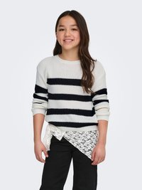 Maglione a maglia con righe blu navy e bianche, scollo rotondo e polsini a coste, sovrapposto a uno strato sottostante in pizzo bianco. Completa il look un paio di pantaloni neri.