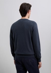 Pulover bleumarin cu decolteu rotund, manșete și tiv drepte, realizat dintr-un material moale. Purtați peste pantaloni din catifea de culoare închisă, cu un detaliu de buzunar în spate.