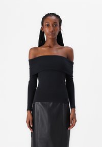 Crna off-shoulder majica s dugim rukavima izrađena od mekog materijala. Ima drapirani izrez i uski siluetu. Uparena s crnom kožnom suknjom.
