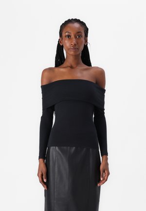 Top negro de manga larga y sin hombros hecho de una tela suave. Presenta un escote drapeado y una silueta ajustada. Combinado con una falda de cuero negra.