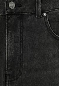 Jeans de mezclilla negra con un primer plano de la textura de la tela, detalles de los botones y un diseño estándar de cinco bolsillos.