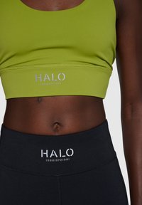 Grøn sportsbh med sølv "HALO" logo,parret med sorte højtaljede leggings med det samme logo, glat stof og tætsiddende design.
