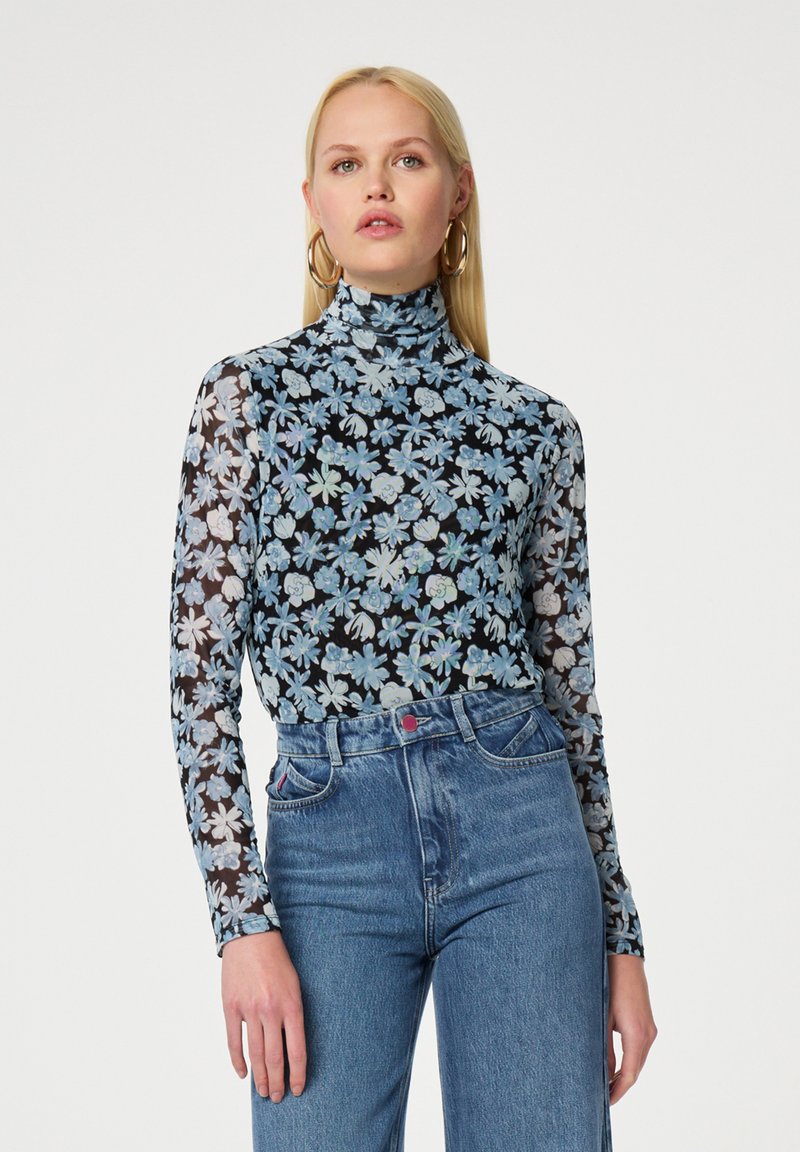 Langsleeve turtleneck top in doorschijnend zwart gaas met een bloemmotief in blauw en wit. Gepaard met hoge blauwe spijkerbroeken.