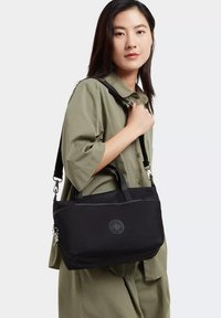 Borsa a spalla nera realizzata in materiale resistente, con manici doppi, una tracolla removibile e un logo rotondo in rilievo su un lato.