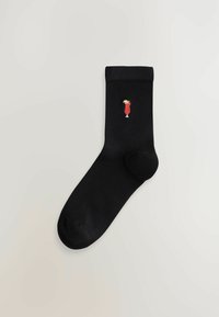 Mustad puuvillane sokk, mille küljes on väike punane kokteiliklaasi tikand, mille jooki kaunistab kollane lõikeaktsent.