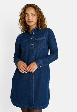 Vestido camisero de mezclilla en azul oscuro con mangas largas, cuello, dos bolsillos frontales y cierre de botones. Presenta un dobladillo curvo y detalles de costura.