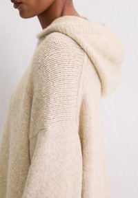 Pull en tricot beige avec capuche, mélange de motifs de points texturés et coupe décontractée. Tissu doux au look confortable.