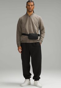 Veste bomber zippée gris clair, banane noire, joggers noirs avec poignets côtelés et baskets blanches. Tissu lisse, design minimal.