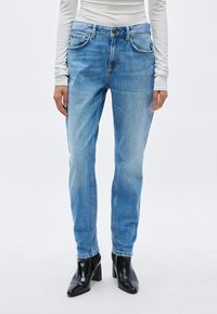 Vaqueros de mezclilla azul claro con corte recto, cinco bolsillos y un desgaste sutil. Combinados con botas negras de tacón.