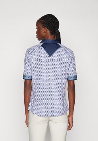 Short-sleeved polo shirt with a geometric pattern in pink and blue. Navy collar and sleeve accents; lightweight, breathable material.