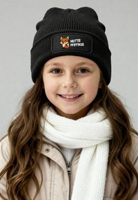 Black knitted beanie with a rectangular patch featuring a fox graphic and the text "MUTTIS PFIFFIKUS." Worn with a white scarf and jacket.