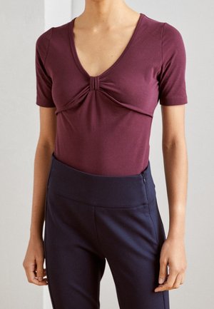 Bordowy top z krótkim rękawem o głębokim dekolcie w kształcie litery V, z ozdobnym skręconym węzłem z przodu, zestawiony z ciemnogranatowymi legginsami z wysokim stanem.