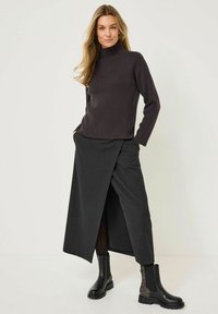 Un pull col roulé côtelé foncé associé à une jupe grise à rayures et fente haute, ainsi qu'à des bottines noires avec des accents texturés sur les côtés.