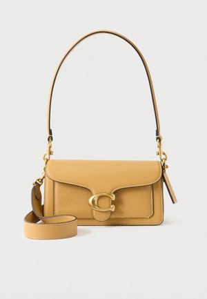 Sac à épaule en cuir fauve avec une fermeture dorée en forme de "C", une bandoulière plus longue amovible et une texture grainée sur un fond clair.