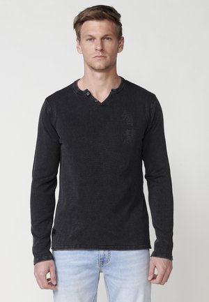 Camisa henley de manga larga negra con un acabado texturizado, que presenta un cuello en v, cierre de dos botones y sutiles toques de marca en los laterales.