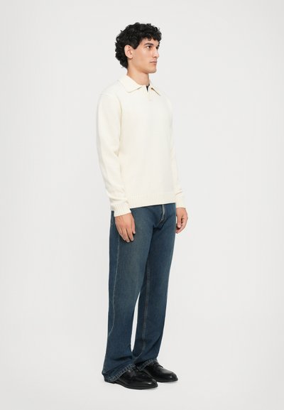 Suéter de crema claro con cuello, tejido texturizado. Combinado con jeans de pierna recta azul oscuro y zapatos negros. Estilo simple y moderno.