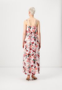 Long floral dress with thin straps, featuring a light pink background, multicolored floral pattern, and a gathered waistline.