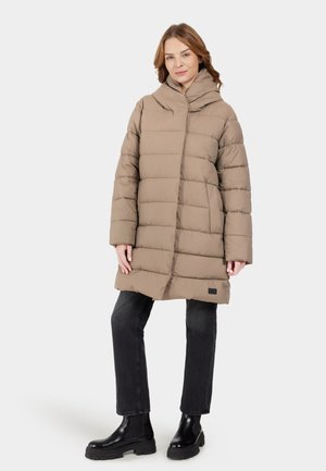 Langer beiger Puffer-Mantel mit Kapuze, der horizontale gesteppten Abschnitte aufweist. Kombiniert mit schwarzen Jeans und klobigen schwarzen Stiefeln.
