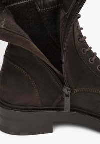 Brązowy zamszowy botek za kostkę o fakturowanym wykończeniu, z bocznym zamkiem błyskawicznym i zaokrąglonym czubkiem. Akcentowany szczegółowym przeszyciem i niskim obcasem.