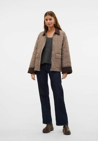 Quiltet brun jakke med en mørkebrun krave og manchetter, parret med en grå sweater og mørke jeans, båret med kraftige brune støvler.