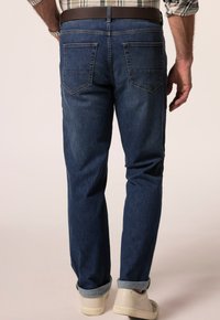 Džínové kalhoty s rovný fit, tmavě modré barvy, dvěma zadními kapsami a ohrnutým lemem. Doplňeno světle zbarvenými teniskami.