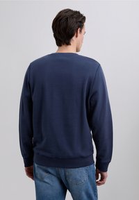 Mörkblå sweatshirt i mjukt tyg med rund halsringning, långa ärmar och ribbstickade muddar. Kombinerad med ljusblå jeans i denim.