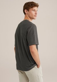 Tmavě šedé tričko s krátkým rukávem a texturovaným designem ve vaflovém pletení. Kulatý výstřih a mírně volný střih, kombinující se s světlými kalhotami.