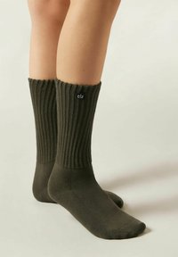 Olivgrüne gerippte Socken mit umgeschlagenem Bund und einem schwarzen Logoakzent. Hergestellt aus weichem Stoff, mit glatter Textur und tailliertem Schnitt.