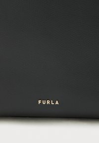 Μαύρη δερμάτινη τσάντα χειρός με υφή και ανάγλυφο χρυσό λογότυπο "FURLA" στο κάτω μέρος. Δεν εμφανίζονται μεταλλικά στοιχεία ή επιπλέον διακοσμητικά.
