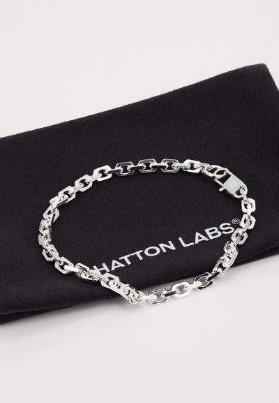 Silver chain bracelet with interlocking hexagonal links, featuring a secure clasp, displayed on a black fabric background with "HATTON LABS" logo.