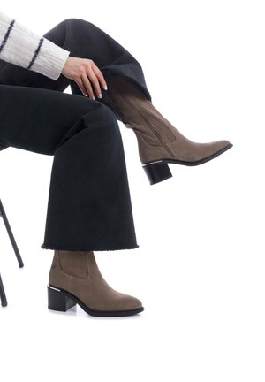 Un par de botines de ante topo con puntera afilada y tacón cuadrado, combinados con pantalones negros de pierna ancha con dobladillo deshilachado.