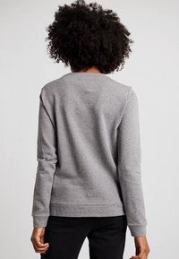 Sweat-shirt gris à manches longues, col rond, texture douce et poignets élastiques. Présente un design simple et épuré sans logos ni motifs visibles.