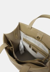 Sac fourre-tout en cuir beige avec une texture lisse. L'intérieur comprend une poche zippée et des poches plaquées ; des accents en métal doré.