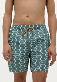 Shorts de bain en teal et crème, dotés d'un motif courbe répétitif. Taille élastique avec cordon de serrage ; tissu léger.