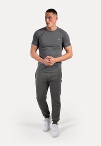Camiseta atlética gris con mangas raglán, combinada con pantalones de chándal gris oscuro. Zapatillas blancas completan el atuendo. Diseño simple, sin patrones.