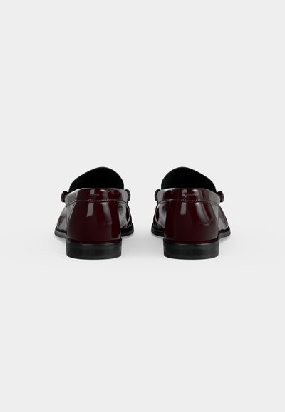 Paire de mocassins en cuir bordeaux foncé et brillant, vue de dos sur un fond uni gris clair.