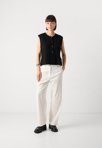 Svarte ermeløse skjorte med knapper laget av teksturert stoff, sammen med off-white vide bukser med vertikale striper, og svarte platåhæler.