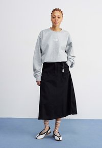 Felpa grigia con logo, gonna lunga nera e scarpe bianche e nere con cinturini incrociati. Tessuto morbido, vestibilità rilassata, design semplice.