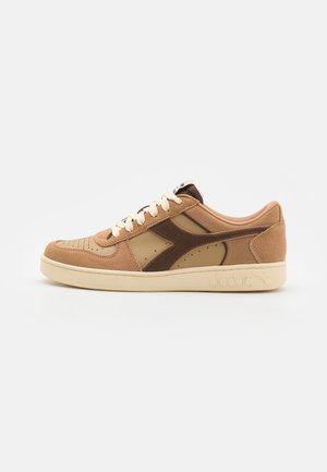 Brown and tan sneaker made of suede and leather. Features perforated toe, cream laces, and a rubber sole with logo detail on the side.