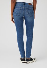 Jeans de mezclilla azul delgados con una cintura alta, que cuentan con dos bolsillos traseros con un distintivo patrón de costura en forma de chevron y un desvanecimiento mínimo.