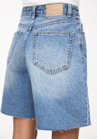 Jeansowe szorty z jasnoniebieskim gradientem, postrzępionym dołem i dwoma tylnymi kieszeniami. Skórzana metka na pasie z nazwą marki.