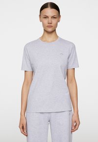 Jasnoszara bawełniana koszulka z okrągłym dekoltem i krótkimi rękawami. Posiada subtelny detal logo na piersi oraz luźny krój.