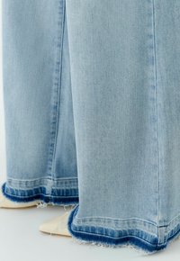 Hellblaue Jeans mit weitem Bein und ausgefranstem Saum, mit zweifarbigem Finish am unteren Rand und einer sauberen vertikalen Naht entlang der Seiten.