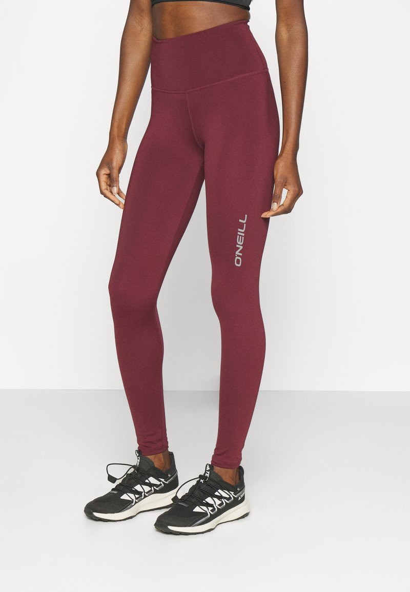 Frau in hoch taillierten weinroten Leggings mit "O'NEILL"-Logo auf dem Oberschenkel und schwarzen Sneakers mit weißen Akzenten.