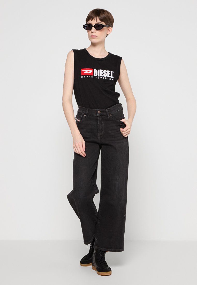 Camicetta nera senza maniche con logo Diesel, abbinata a pantaloni in denim neri a vita alta e larghi. Accentuata con scarpe nere stringate e occhiali da sole.