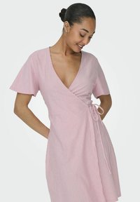 Robe portefeuille à rayures rose et blanche avec des manches courtes, décolleté en V, détail de lien sur le côté et texture de tissu douce. Longueur mi-cuisse.