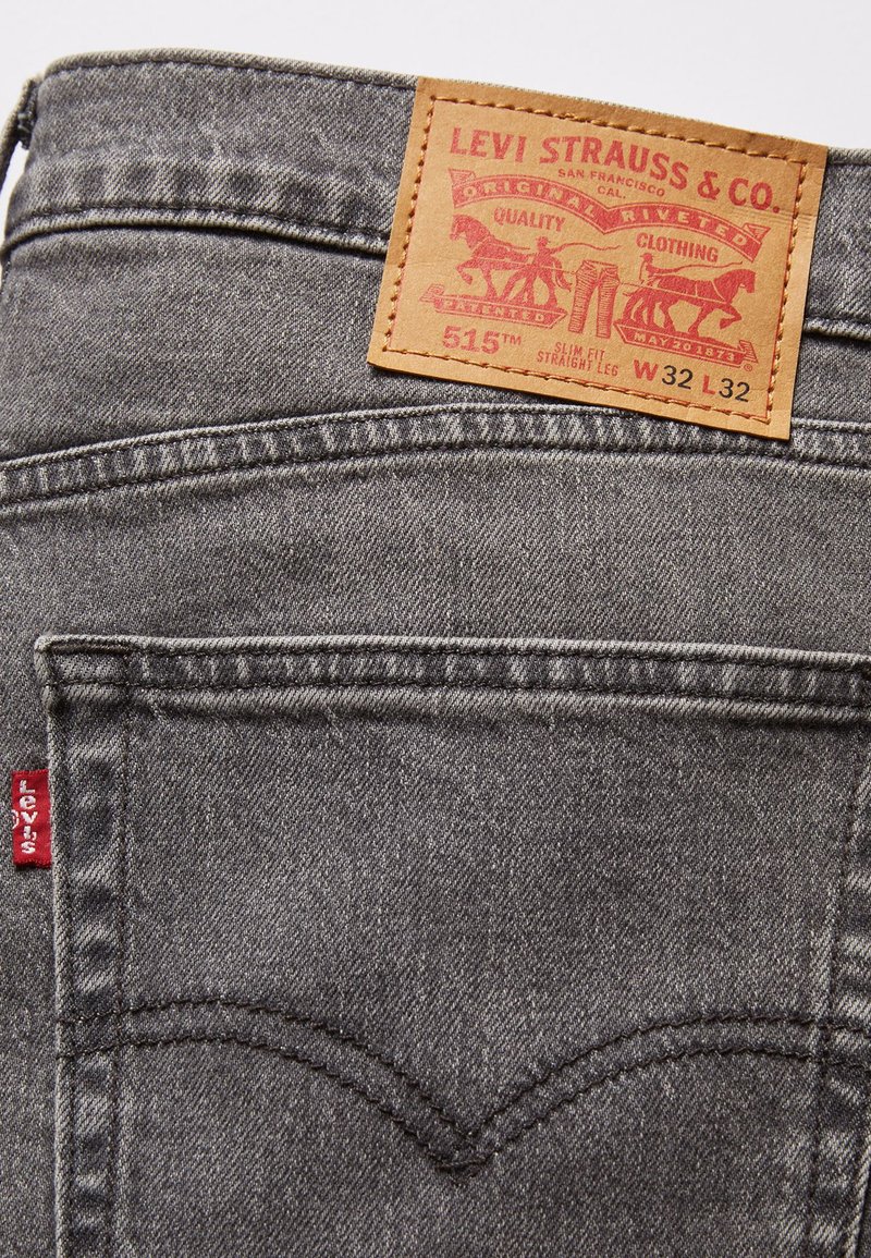 Jeans de mezclilla gris con una etiqueta de cuero que dice "Levi Strauss & Co." y "515" adherida a la cinturilla. Presenta una pestaña roja en el bolsillo.