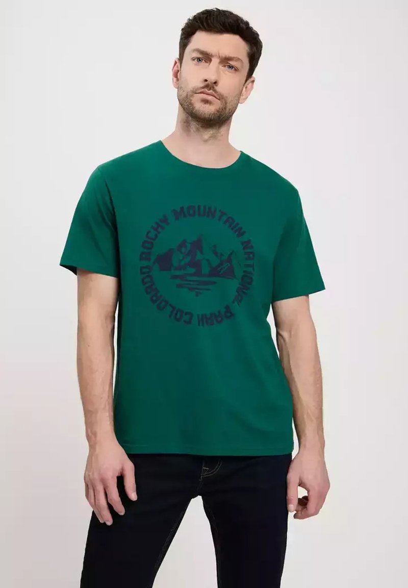 Zielona bawełniana koszulka z krótkimi rękawami, z okrągłą grafiką gór i tekstem w ciemnoniebieskim kolorze. Projekt z okrągłym dekoltem, luźny krój.